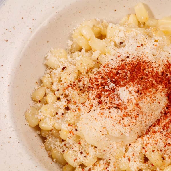 Close-up of Mexican street corn (Esquites) with mayonnaise, cheese, and chili powder in a bowl.